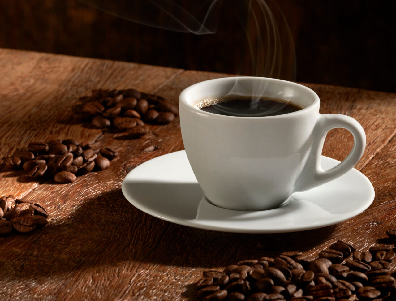 Xícara de café com grãos torrados e selecionados em fundo de madeira rústica, na vertical.