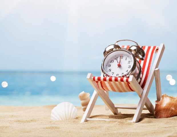 Last Minute Urlaub, Liege mit Uhr drauf am Strand