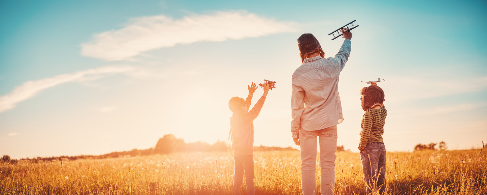 Tipps gegen Flugangst, Vater mit zwei Söhnen auf einem Feld, jeder hält ein Flugzeug in der Hand
