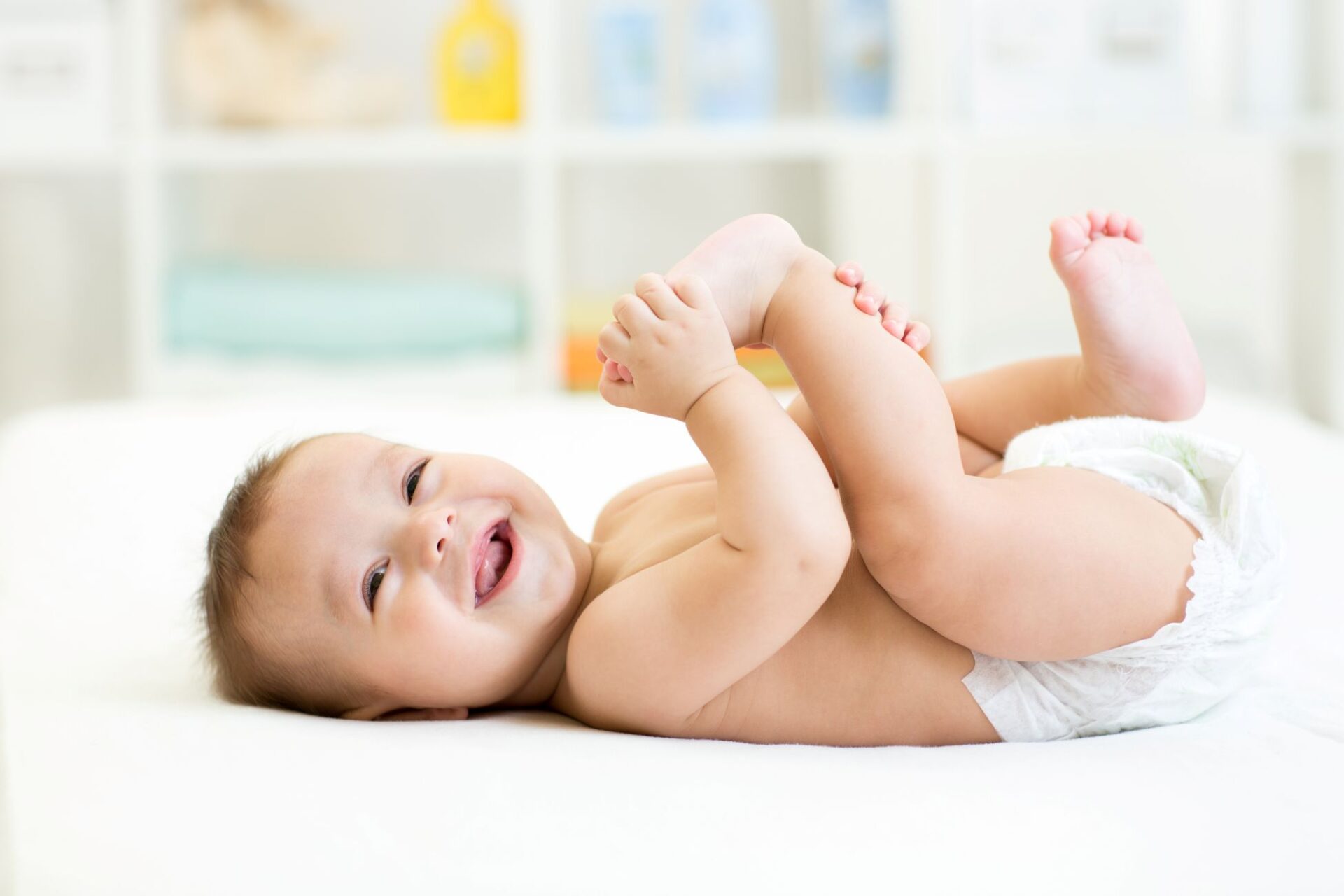 Lachendes Baby mit Windel liegt auf weißer Wickelunterlage
