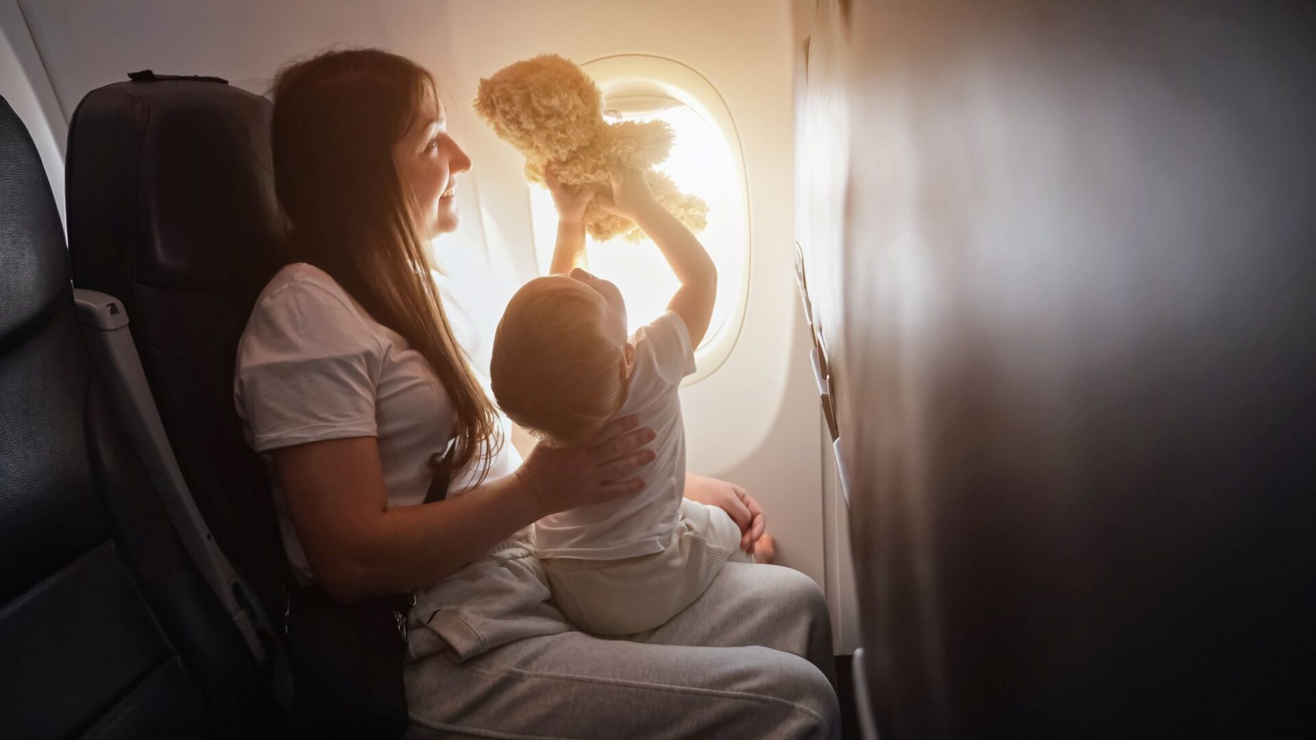 Mutter mit Kleinkind und Teddy am Fensterplatz im Flugzeug